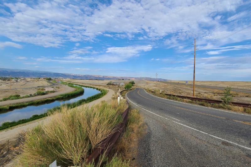 Road and body of water next to each other with blue sky and white clouds above. 