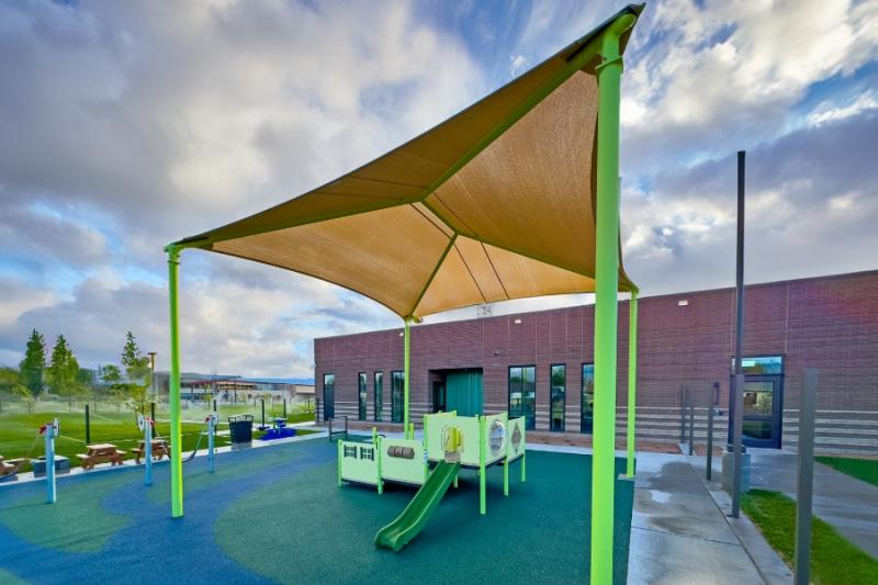Green and tan outdoor canopy over green playground. 
