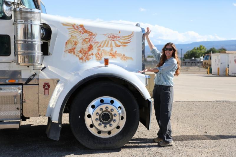 Woman standing with her arms displaying a large semi truck. 