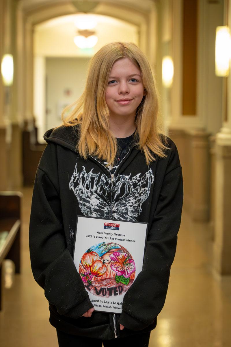 Middle school student holds up plaque with her winning "I Voted" Sticker Design. 