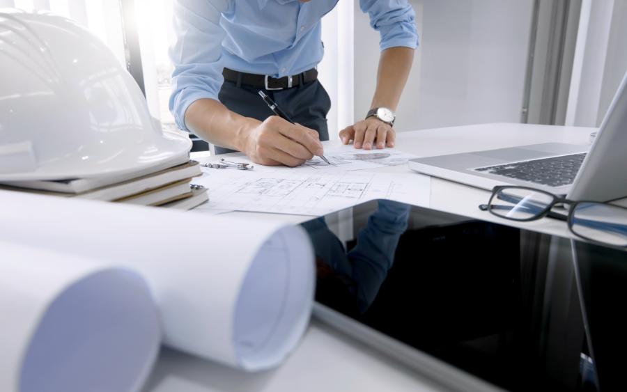 Photograph of Engineer working on blue prints on a desk with laptop