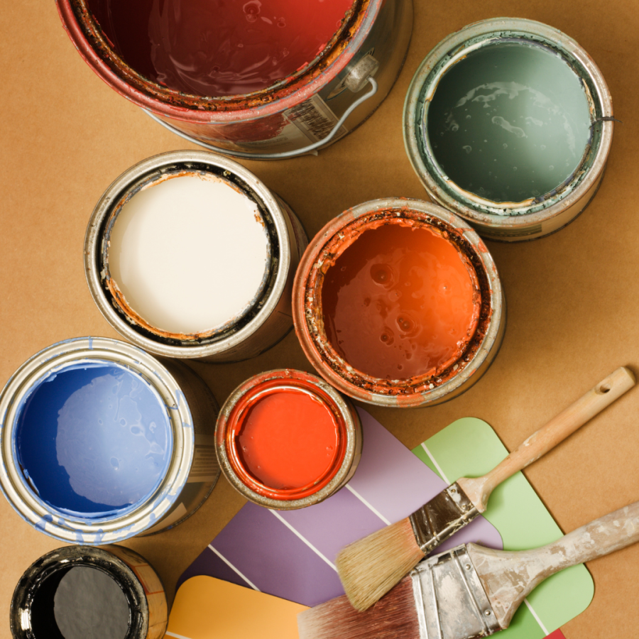 Open cans of vibrant paint with brushes around them.