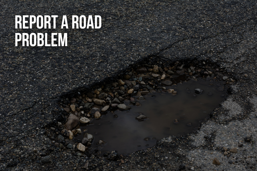 Dark image of pothole in road reading "REPORT A ROAD PROBLEM" at the top left of the image in white font.