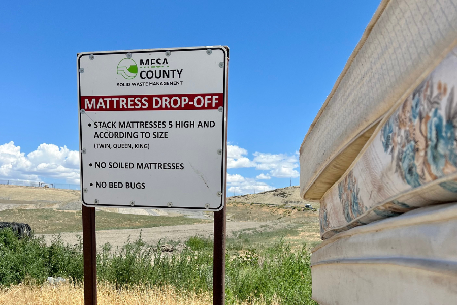 Stacked mattresses next to Mesa County Landfill sign.