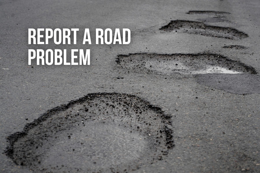 Potholes on road with white text reading "REPORT A ROAD PROBLEM".