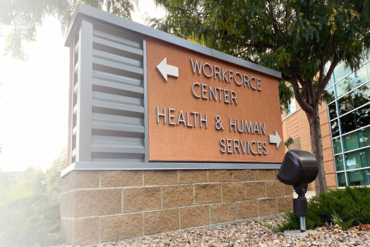 Image of a brick sign outside of a building. The sign reads has arrows pointing to the Workforce Center and Health & Human Services.