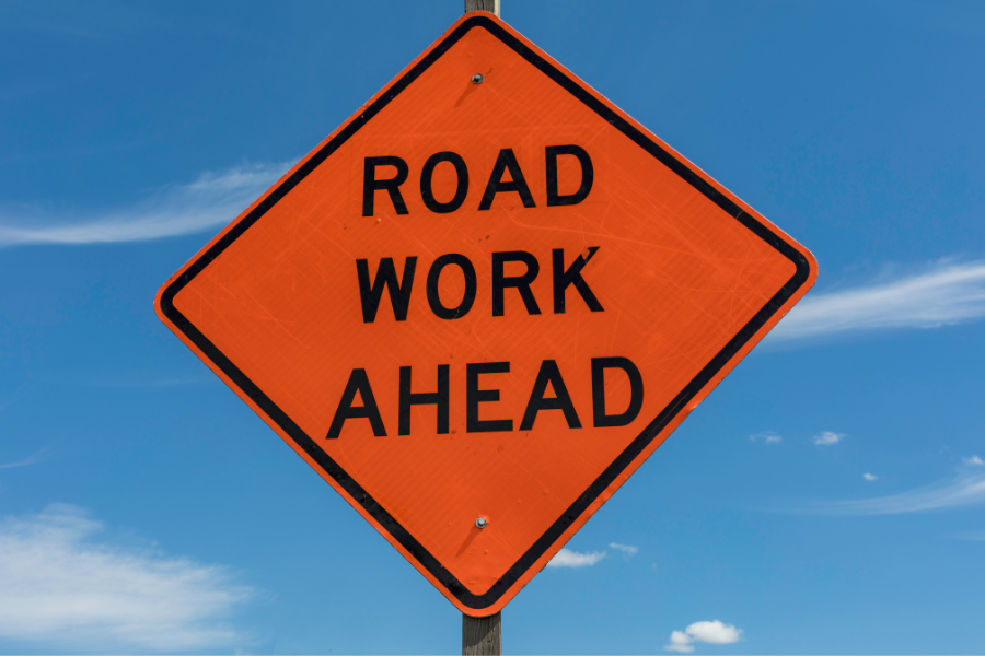 Bright orange diamond shaped sign with black text reading, "ROAD WORK AHEAD"