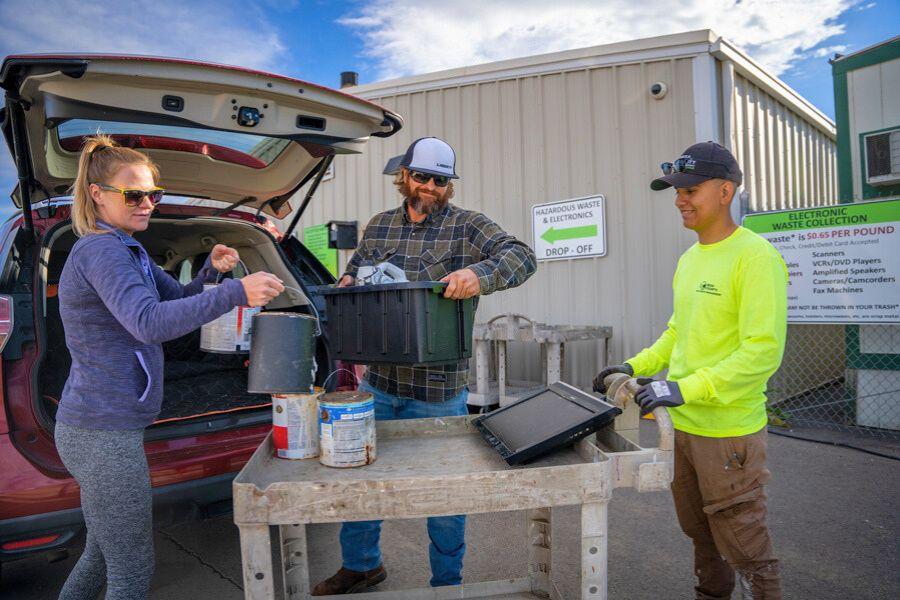Three people unload paint, electronics, and other toxic household items from a red car onto a grey cart at the Mesa County Hazardous Waste Collection Facility. 