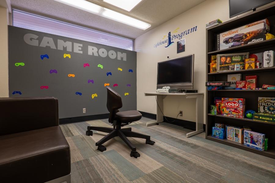 Room full of games and a large tv screen with "Game Room" and the Lighthouse Program logo on the wall. 