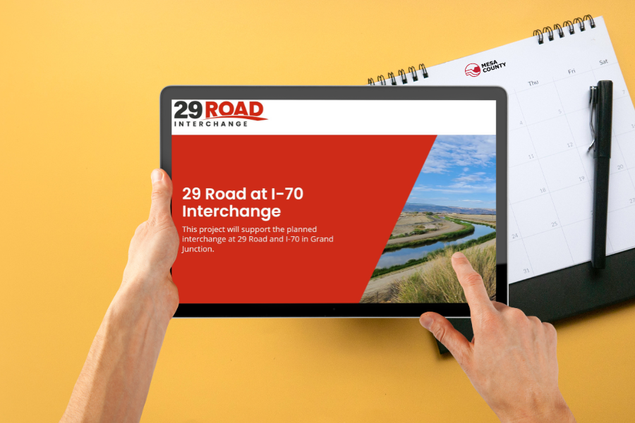 Yellow background with part of a calendar showing and two hands holding an IPad displaying an invite with a red background and white text reading, "29 Road at I-70 Interchange."