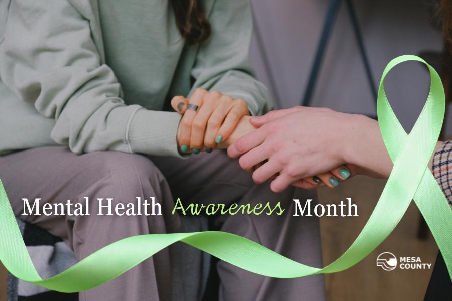 Person's handing holding another person's hand with a green ribbon below and white and green text above it reading, "Mental Health Awareness Month", and the white Mesa County logo on the bottom right. 