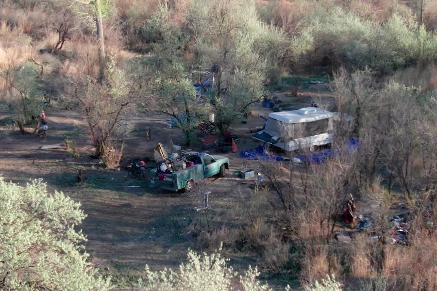 Aerial view of junk, trash, and vehicles on open space surrounded by bushes and trees. 