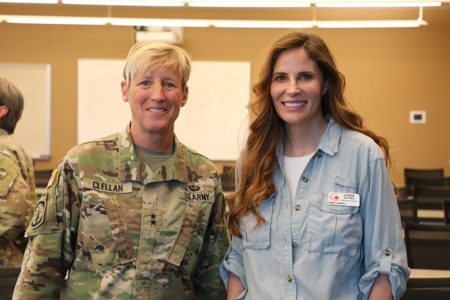 Two women smiling at camera. The woman on the left is wearing an Army uniform. 