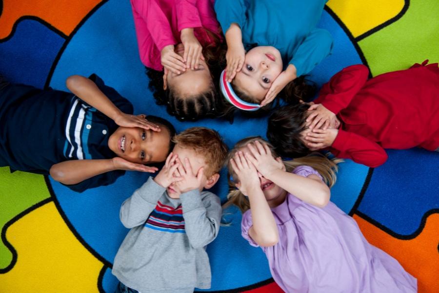 Six young kids laying on colorful carpet. 