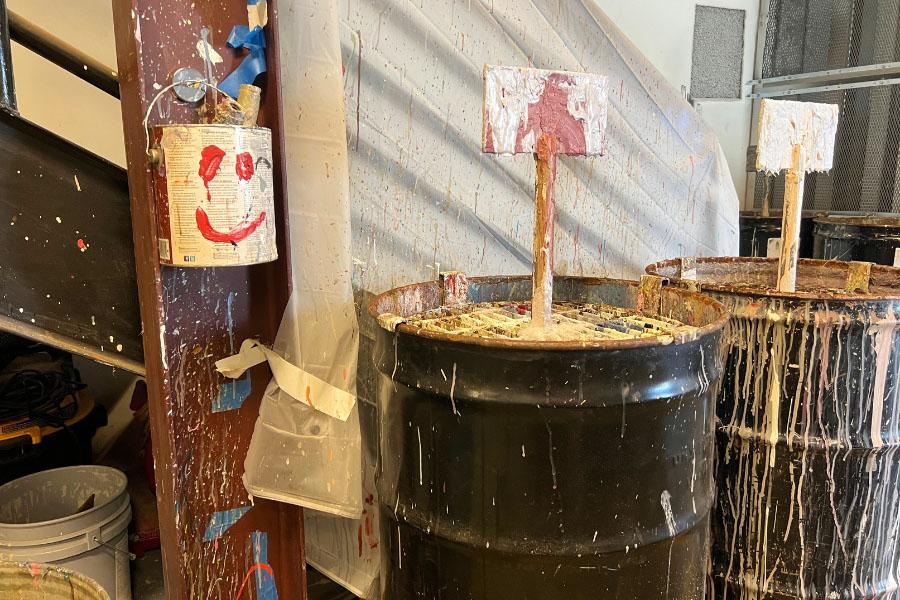 Paint can hanging on wall with red painted smiley face. 