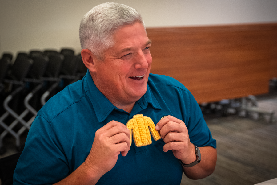 Man in blue shirt holding up yellow sweater cookie to his chest.